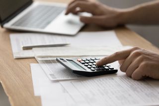 © fizkes - Adobe Stock.com Foto: Person tippt auf Laptop und Taschenrechner